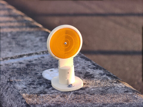Orange road reflector delineator mounted on a concrete kerb at the roadside. Traffic safety close up