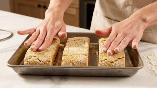 Chef carefully places three rectangular blocks of food in a metal baking pan on a kitchen countertop
