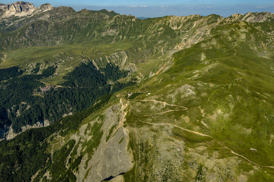 Aerial Alpine Mountain Landscape with Rugged Ridges, Meadow Slopes, Forested Ravine and Winding Unpaved Road