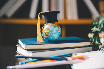 Small world globe in a graduation cap rests on stacked books with colorful pencils nearby, representing global education, international learning, study, knowledge, achievement, and student success