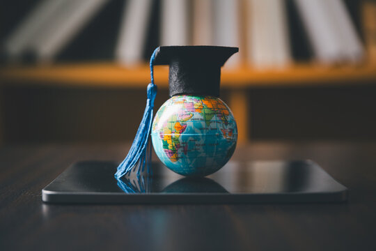 Graduation cap on a small world globe resting on a digital tablet in a library, representing global education, online learning, international study, academic success, knowledge, and technology.