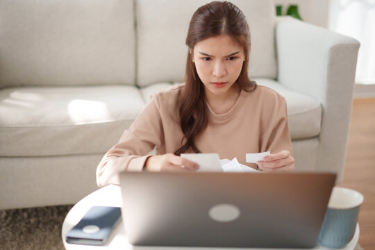 Worried Asian woman reviewing receipts and household bills with a laptop at home, representing monthly expenses, financial stress, payments and personal money management.