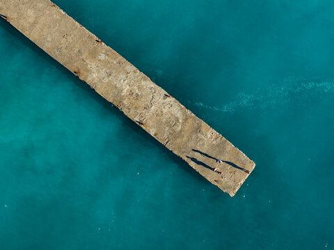 Aerial Concrete Pier Extending into Turquoise Sea with People on Rounded Terminal