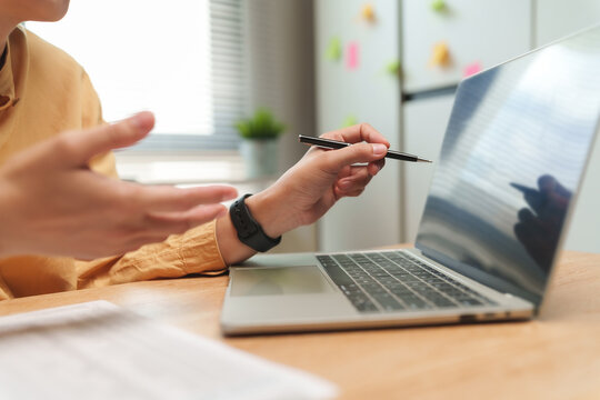 Businesswoman joining a business video call on a laptop while gesturing with a pen, representing remote meetings, online communication, consulting, teamwork and digital workplace collaboration.
