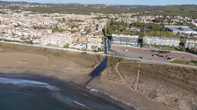 Aerial view of the Mediterranean coastline and sandy beach meeting a drainage stream channel, marking the provincial border between Barcelona and Tarragona, backed by the coastal town of Cunit, Catalo