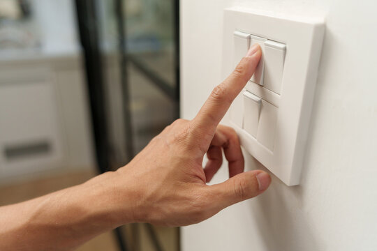 Close-up of a hand pressing a wall light switch at home, representing electricity control, energy saving, power efficiency, reduced consumption.