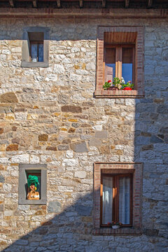 A picturesque architectural detail of a historic building in Castellina in Chianti, Tuscany, Italy. A niche in the wall houses a colorful decorative figurine depicting a stylized human bust.