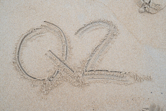 Top-down view of the text Q2 inscribed cleanly into smooth natural beach sand