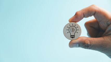 Hand holds a wooden token with a light bulb, brain, and circuit symbol, representing artificial intelligence, creative thinking, innovation, technology, knowledge, learning, and digital solutions. © Manasanan Wongchoomp