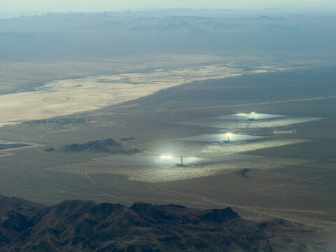 Aerial view of solar thermal plants with bright glowing towers, mirror arrays, and a dry lakebed beyond, Mojave Desert, California