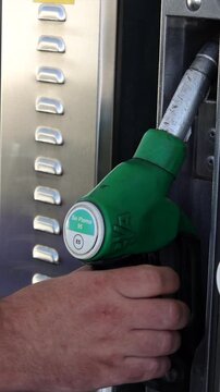 Vertical view of a hand unhooking a fuel pump nozzle at a gas station, symbolizing rising petrol prices, energy inflation, expensive vehicle refuel expenses, and financial strain on drivers.
