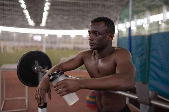 Black sportsman with water resting near barbell