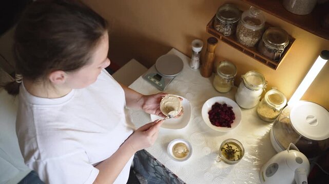 Young woman prepares healthy low carb breakfast in home kitchen. Spreads round whole grain crispbread with hummus paste with nuts. Vegetarian high protein dish for breakfast.