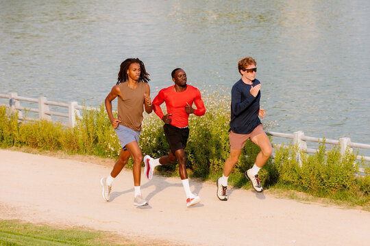 Wide shot of male runners jogging by a park lake.