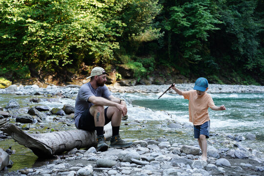 Man Sitting on a Log Watching a Boy with a Stick in the River