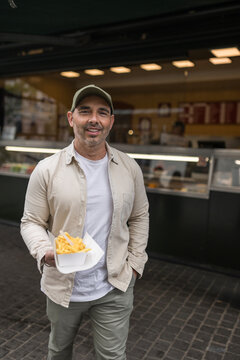 Happy man holding Belgian fries outside food stall