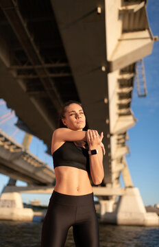 Woman stretching arms standing on seafront under bridge