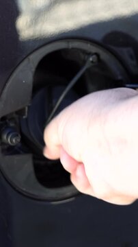 Vertical detailed view of a person hand opening the car gas tank door compartment before refueling with petrol at a fuel pump.