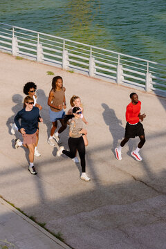 Fitness friends jogging together by a sunny urban park lake.