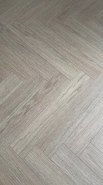 Vertical 4K video showing a static diagonal top-down view of a natural oak parquet floor laid in a classic herringbone pattern. Features a modern grey-beige wood texture and grain.