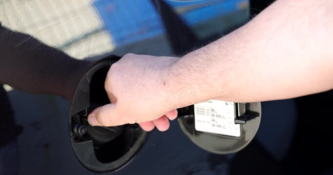 Horizontal macro detail of a driver hand closing the fuel door cap on a vehicle after filling up the tank at a service station.
