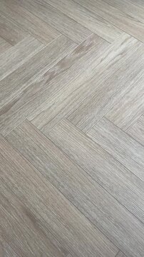Vertical 4K video showing smooth camera motion panning over a light oak parquet floor in a classic herringbone pattern. Highlights the modern grey-beige wood texture and subtle natural grain.