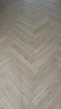 Vertical 4K video showing a smooth light sweep moving across a natural oak parquet floor laid in a classic herringbone pattern. Highlights the warm grey-beige tone and detailed wood texture. 