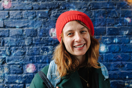 Smiling woman wearing red beanie in front of blue brick wall