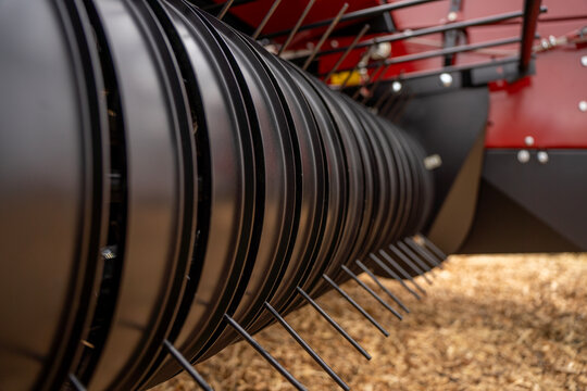 Close-up view of rotating pick up drum with steel tines on agricultural baler machine for harvesting hay and straw.