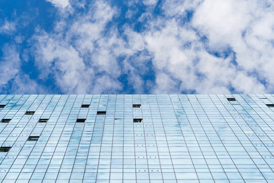 Low angle view of a modern glass skyscraper facade reflecting sky against white clouds