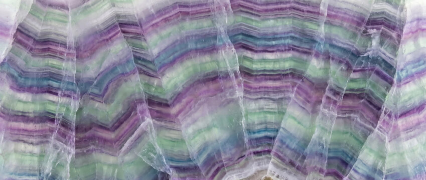 Banded fluorite mineral specimen texture. Macro slice of colorful purple and green crystal layers with chevron banding pattern