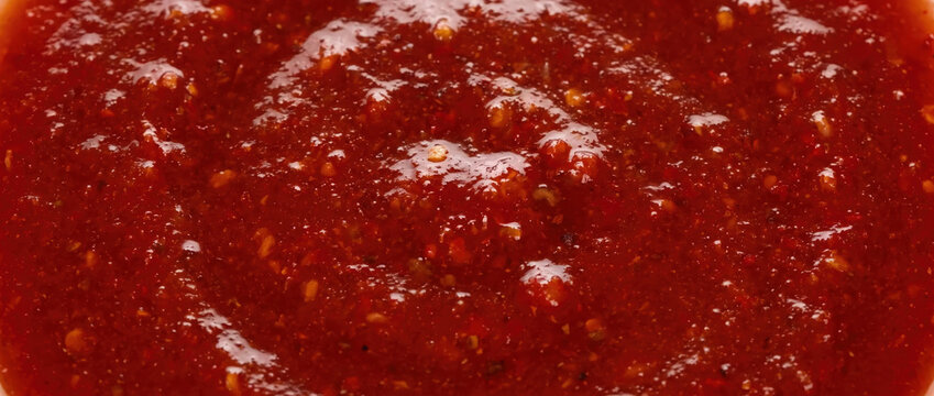 Close up of red hot sauce texture. Glossy chili paste liquid background. Spicy food ingredient detail