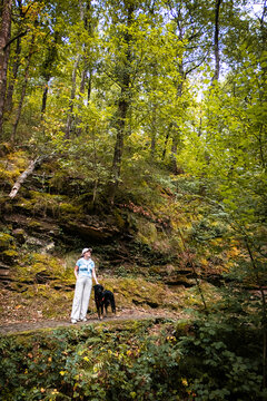 Woman walking with her black dog in an autumn forest