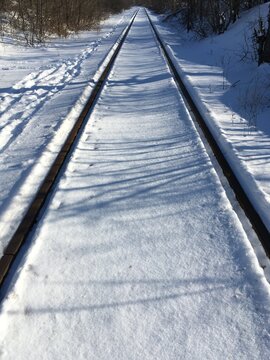 Winter rail road covered with fresh white snow - smooth untrodden surface with no footprints surrounded with bare trees and bushes; linear perspective photo for New Year inspiration, path to discovery