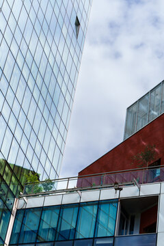 Low angle view of modern glass skyscraper and urban building facade against a cloudy sky.
Low angle view of modern glass skyscraper and urban building facade against a cloudy sky.