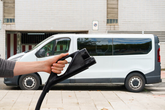 A person holding an electric vehicle charging plug in front of a white commercial van
