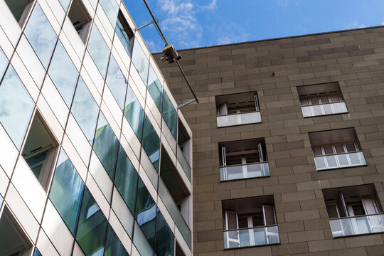 Low angle view of modern glass modern office building next to a tiled residential building facade