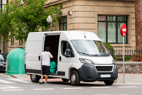 A courier unloading packages from the sliding side door of a white commercial van on a city street