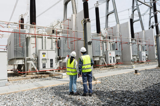 Scheduled transformer inspection at the substation involves two technicians in hard hats pointing at the power transformer and its radiator.