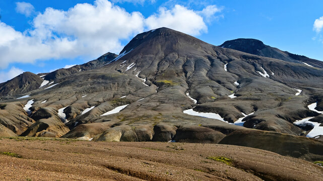 A dark volcanic peak with deep erosion ridges and lingering snow rises above a barren plain near Kerlingarfjoll, Icelandic highlands.