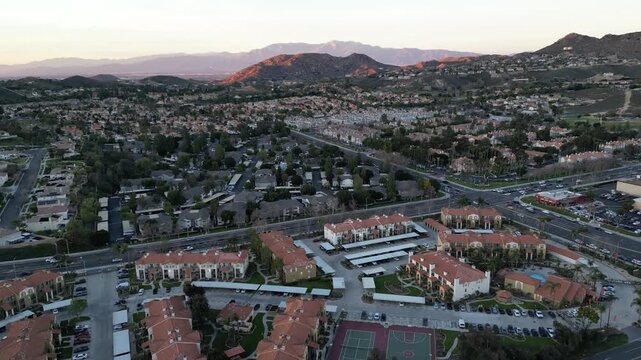 Aerial towards hills and over residential neighborhoods and streets in Corona, California during sunset. Located in Riverside County, in the Inland Empire near Los Angeles. Shot during January, 2024.