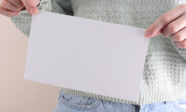 Woman in jeans holding a white blank sheet of paper on a beige background