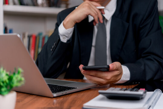 Business person checking smartphone beside laptop calculator and documents for budgeting financial planning and mobile office workflow