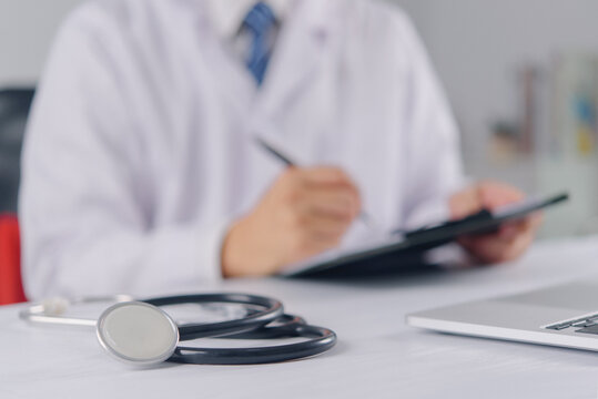 Stethoscope on Medical Desk with Doctor Writing in Background for Healthcare Clinical Practice Diagnosis and Medical Documentation