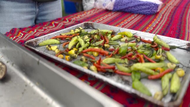 Fresh spicy chili peppers roasting on a metal tray during outdoor food preparation, showcasing vibrant culinary b-roll footage.
