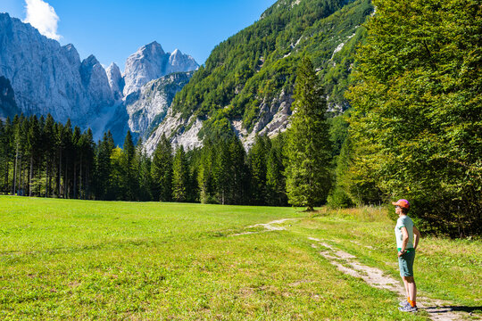 Hiker standing on a meadow trail looking toward the towering peaks of the Julian Alps in Tamar Valley, Slovenia