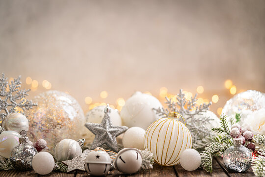 A Christmas background featuring elegant white and silver baubles, glittering stars, jingle bells, and snowflakes on rustic wood, set against a warm backdrop with twinkling lights and copy space.