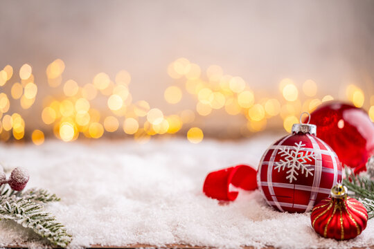 A Christmas background featuring red baubles with golden glitter stripes, a star, and ribbon framing wide snowy ground, softly lit by warm twinkling lights with generous copy space.