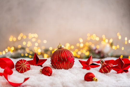 A Christmas background featuring red baubles with golden glitter stripes, a star, and ribbon framing wide snowy ground, softly lit by warm twinkling lights with generous copy space.