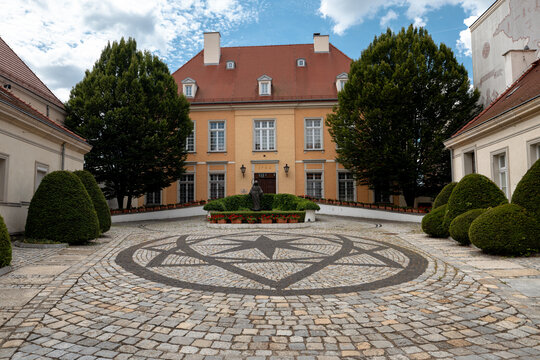 Wroclaw, Poland - July 10, 2026: Formal courtyard on Ostrow Tumski features clipped trees, patterned stone paving and a historic building with a red tile roof.